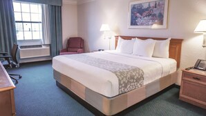 A hotel room with a large bed, a desk, a chair, a radiator, and a painting on the wall. - La Quinta Inn by Wyndham Moline Airport (Moline)