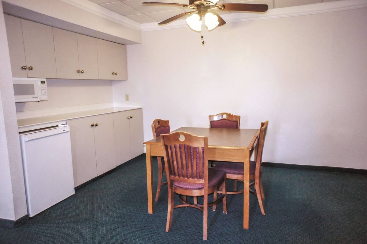 A compact kitchen with a microwave, a small refrigerator, and wooden chairs around a table.