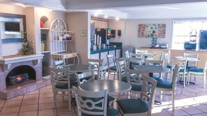 A restaurant with round tables and white chairs, a fireplace, a coffee machine, and a colorful wall decoration. - La Quinta Inn by Wyndham Moline Airport (Moline)