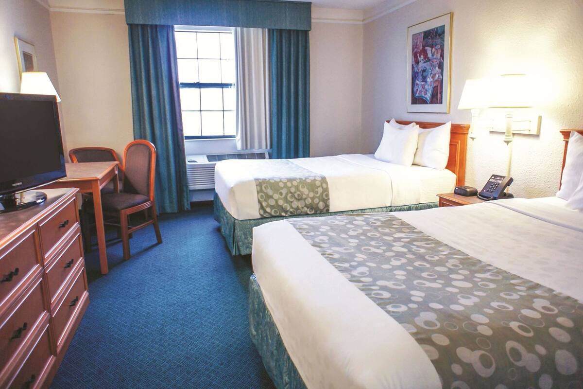 A hotel room with two beds, a desk with a television, a chair, a desk lamp, a telephone, and a painting on the wall.