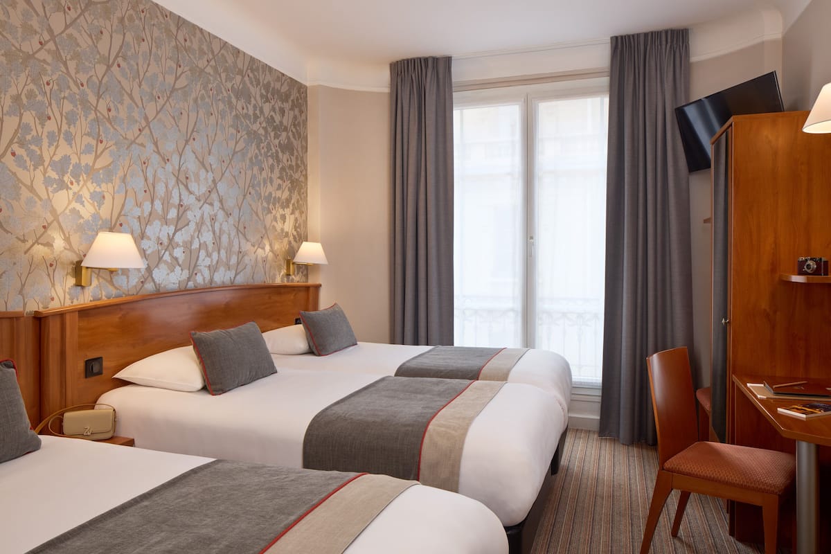 Habitación de hotel con dos camas, un escritorio, una silla, un televisor y una ventana con cortinas.