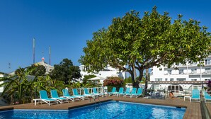 A swimming pool with blue water, surrounded by white lounge chairs and a large tree.