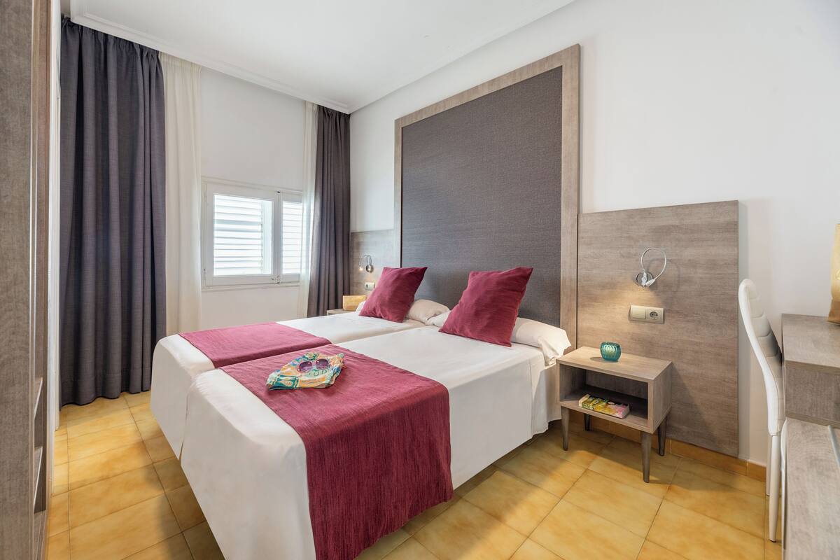 Un lit double avec une couvre-lit rouge, une table de chevet avec une lampe et une petite étagère avec des livres.