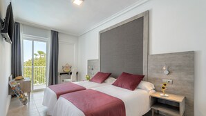 A hotel room with two beds, a TV, a balcony, and a nightstand with a lamp.