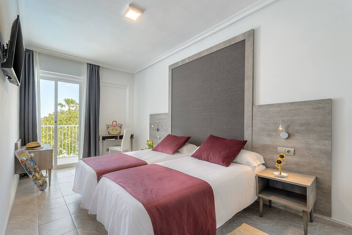 Une chambre d’hôtel avec deux lits, une télévision, un balcon et une table de chevet avec une lampe.