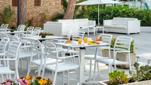 An outdoor patio with white furniture, including tables and chairs, and a stone wall in the background.