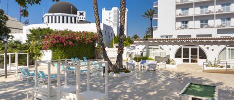 A hotel courtyard with lounge chairs, a pool table, and a building with a dome and balconies.