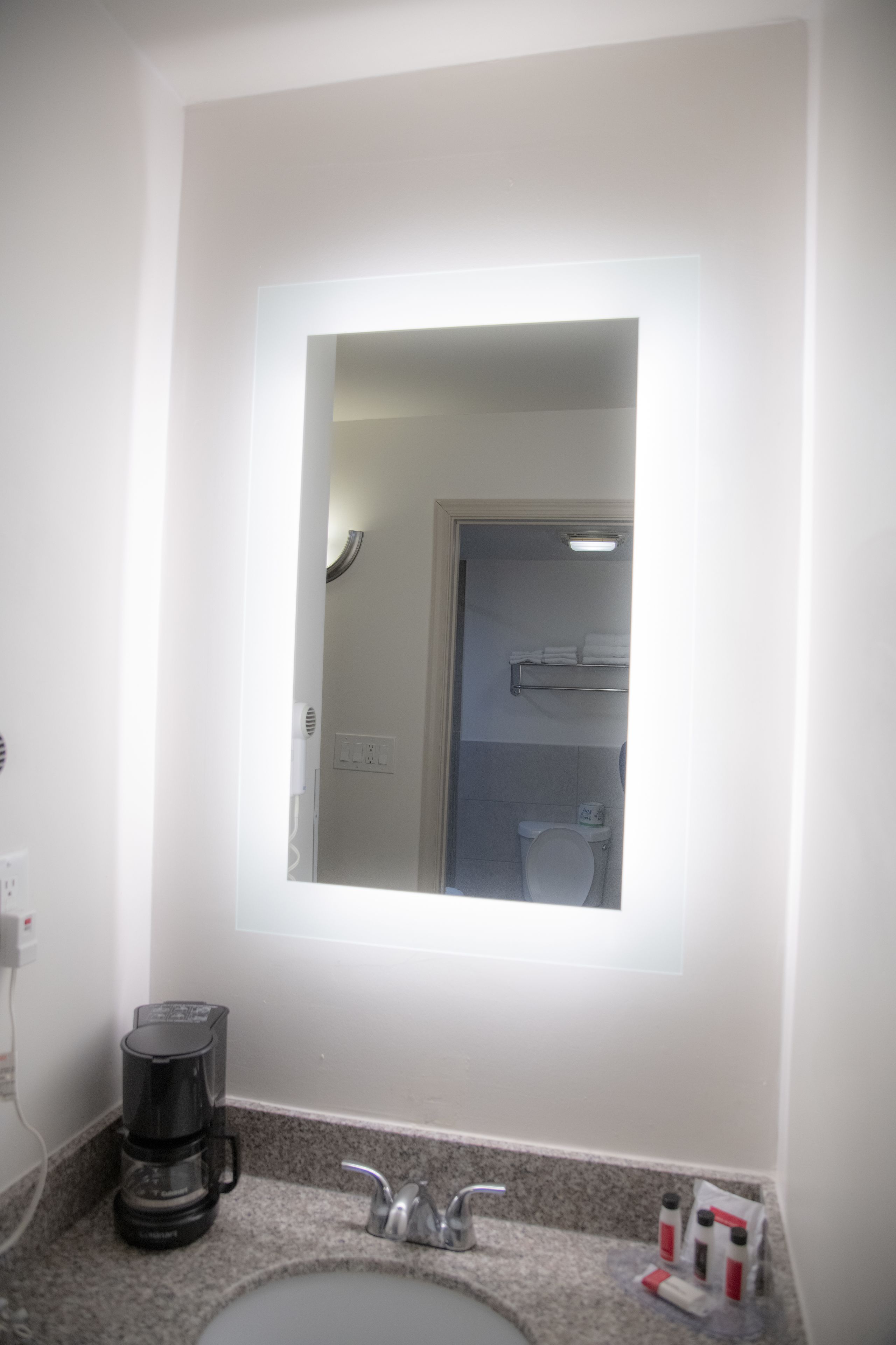 A bathroom with a sink, a mirror, a coffee maker, and a towel rack.