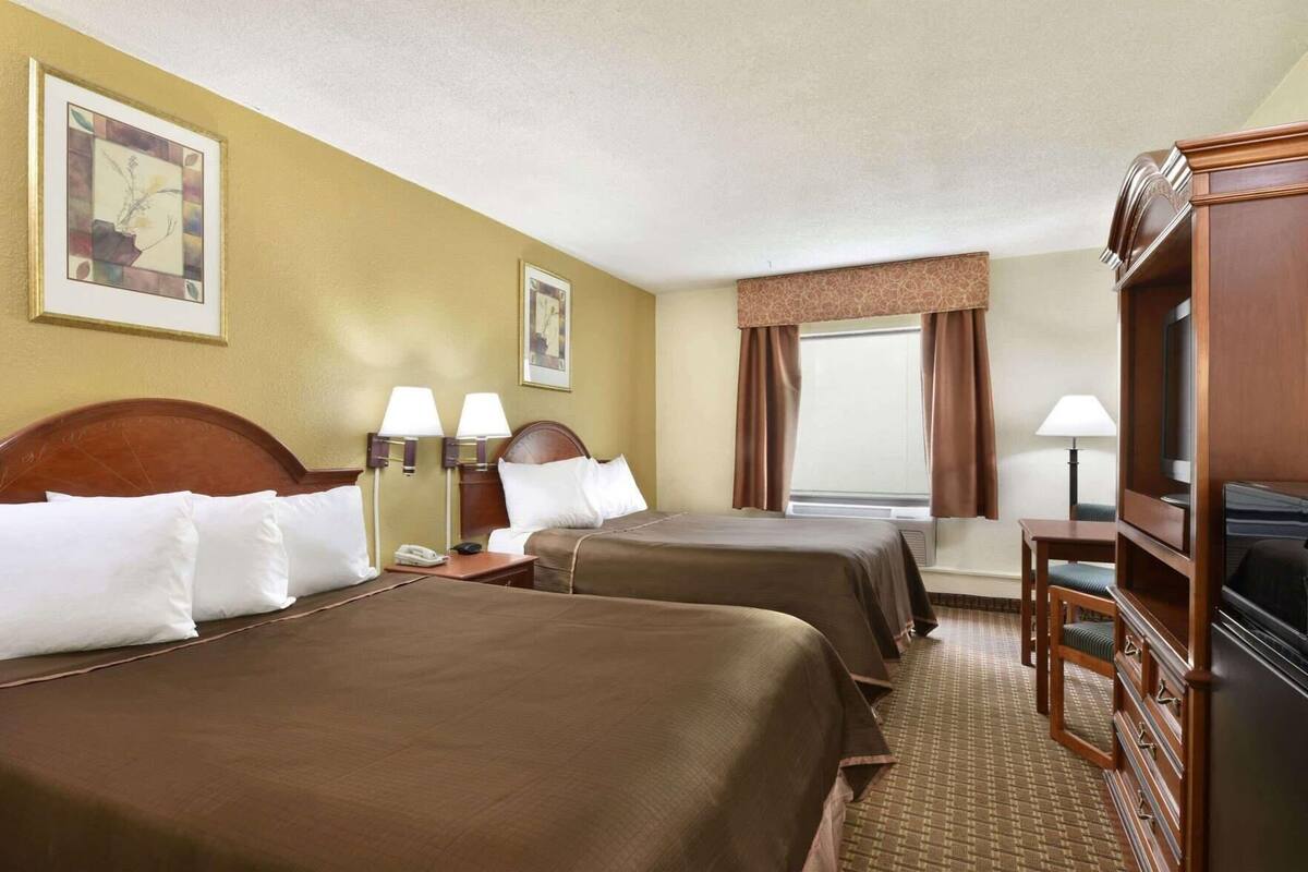 Ein Hotelzimmer mit zwei Betten, einem Fernseher, einem Schreibtisch und einem fenster mit Vorhängen.
