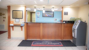 Un mostrador de recepción con encimera de madera, un quiosco digital y una alfombra con la marca 'Howard Johnson'.