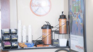 Una estación de café con vasos desechables, una cafetera y un cartel en la pared.