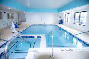 Una piscina con zona poco profonda delimitata, uno spogliatoio con un asciugamano blu e una finestra che si affaccia su auto parcheggiate.