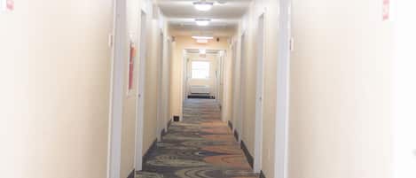 Un pasillo de hotel con pisos alfombrados, paredes blancas y puertas a ambos lados.