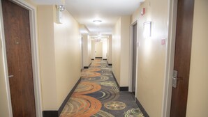 Un pasillo de hotel con alfombra estampada, puertas a ambos lados y una l ámpara en el techo.