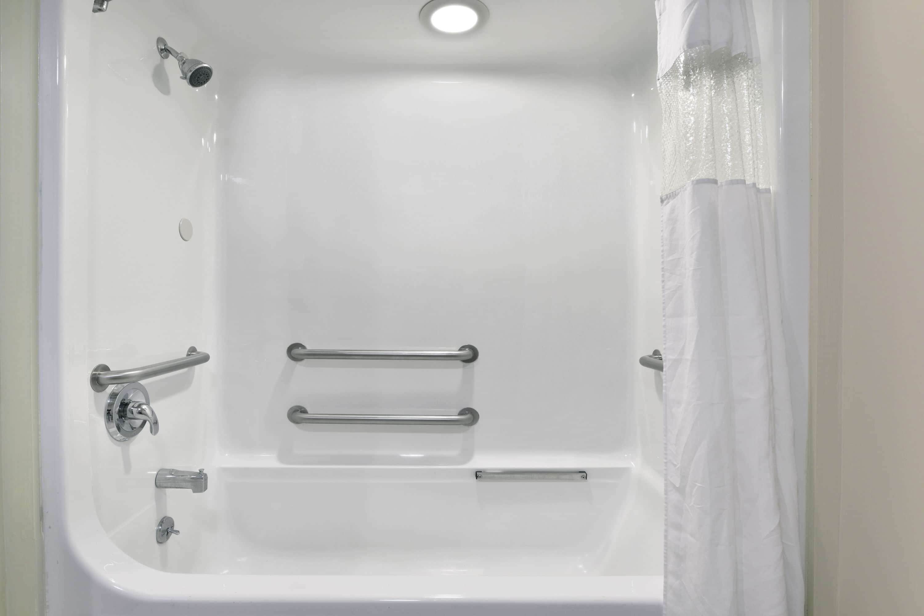 A white bathtub with a showerhead, grab bars, and a curtain.