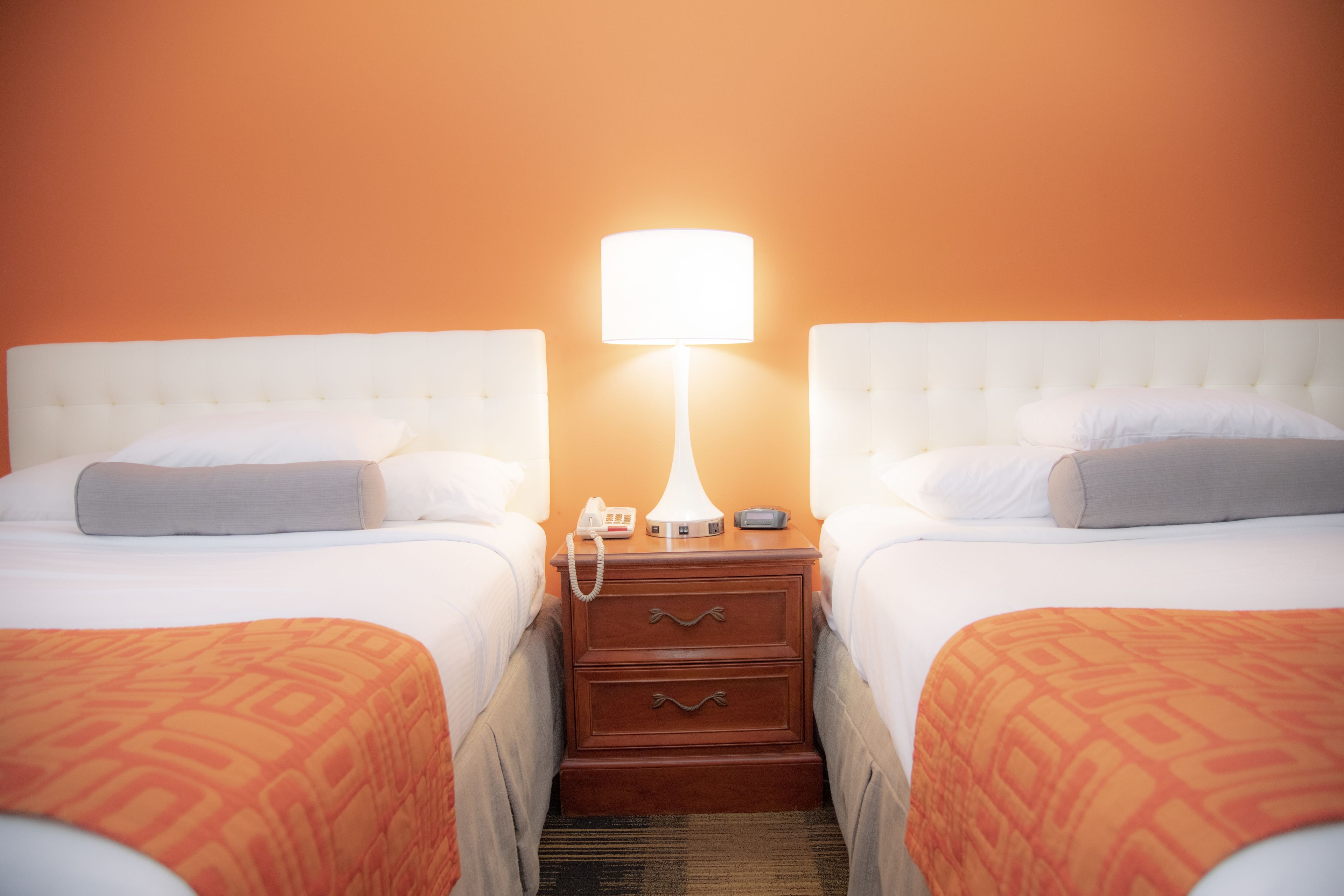 Une chambre d’hôtel avec deux lits, une table de chevet avec une lampe, un téléphone et une horloge numérique.