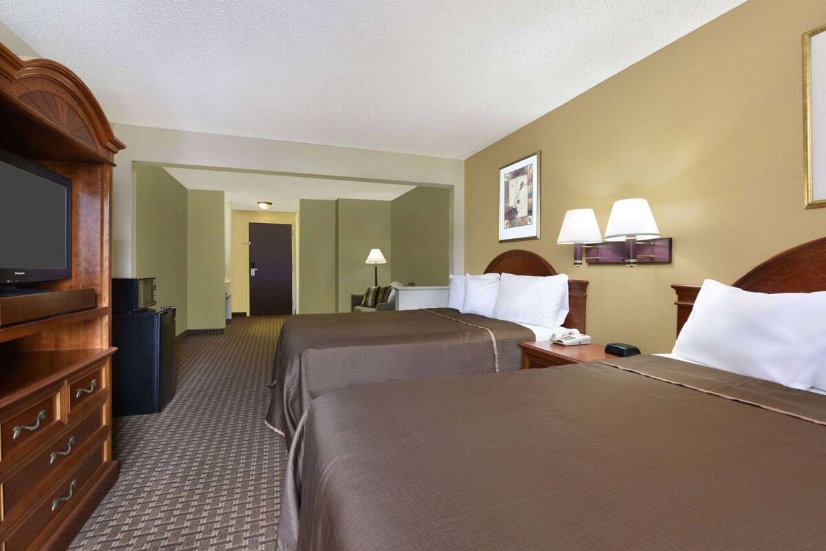 Ein Hotelzimmer mit zwei Betten, einem Fernseher, einem Schreibtisch und einer Lampe.