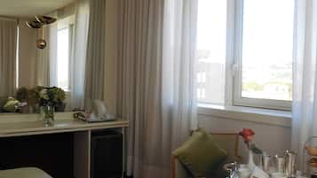 Una camera d'albergo con un letto, una scrivania con il telefono, un vaso con fiori, una poltrona con cuscino e una finestra con tende.