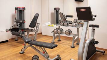Een sportschool met diverse fitnessapparaten, waaronder een bankdrukapparaat, dumbbells en krachttoestellen.
