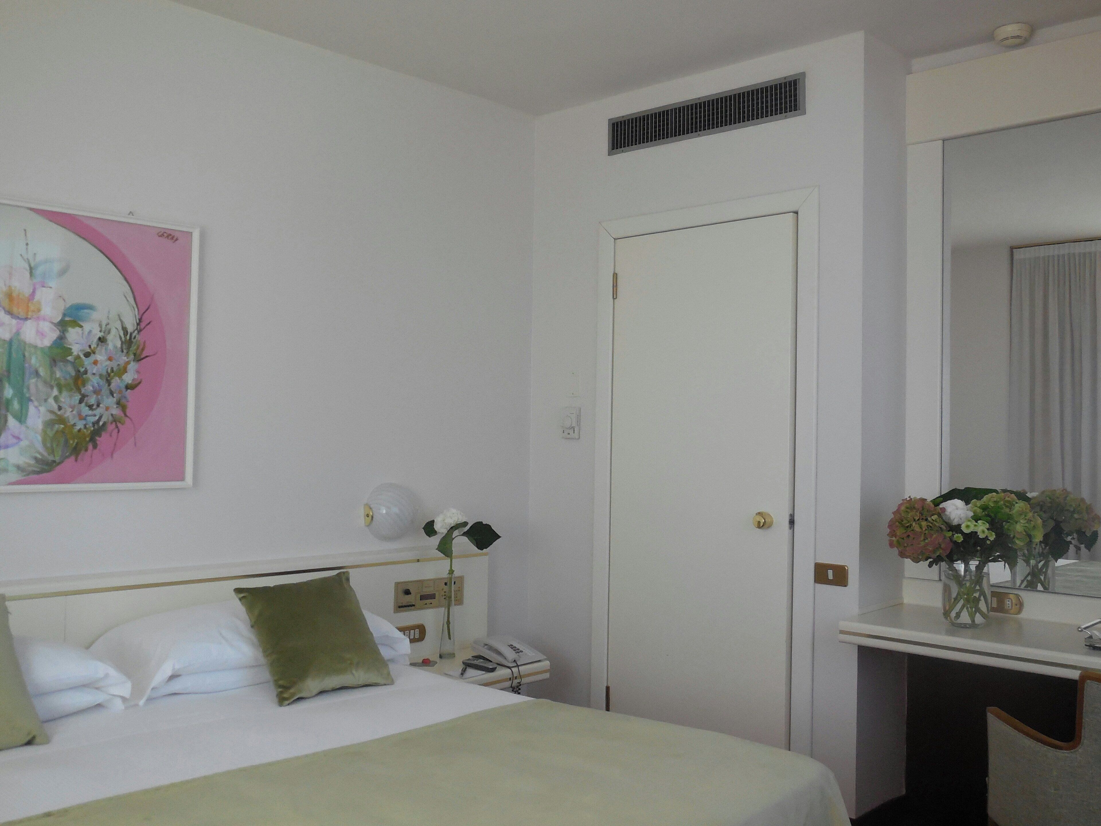 A hotel room with a bed, bedside table, a mirror, a painting, and a door.
