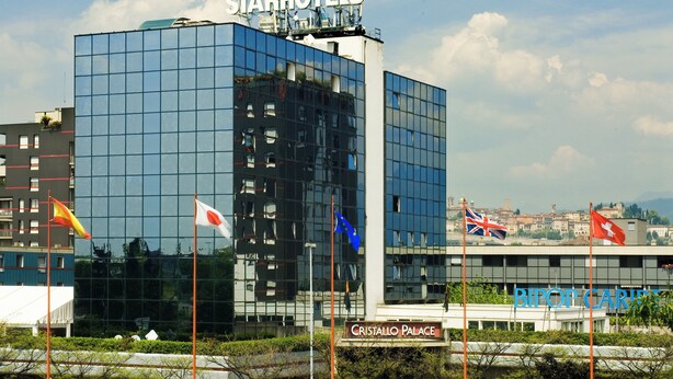 A modern StarHotels building with a glass facade, a sign reading "Cristallo Palace," and multiple flags including the UK and Swiss flags.