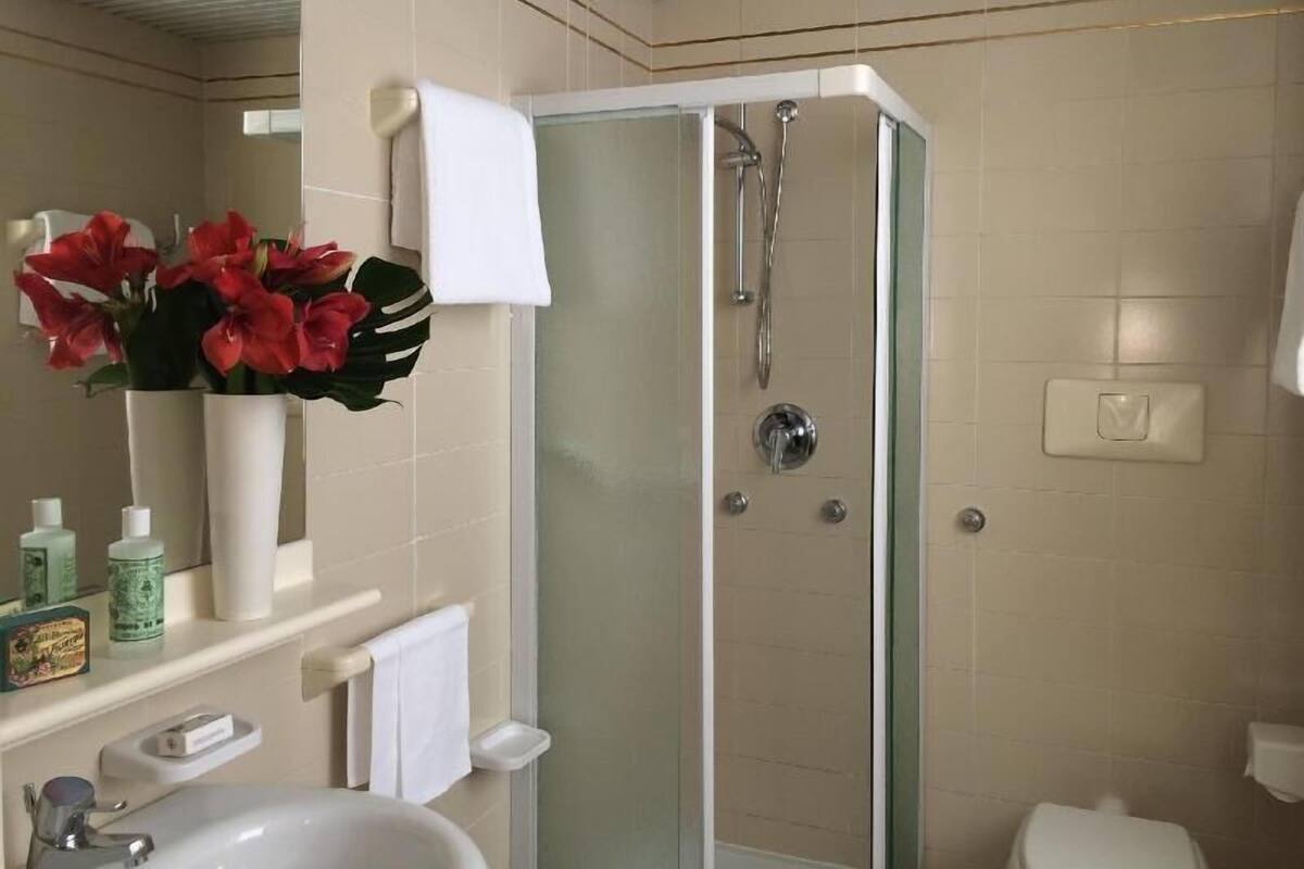 A modern bathroom with a glass-enclosed shower, a toilet, a sink, and a vase with red flowers on the counter.