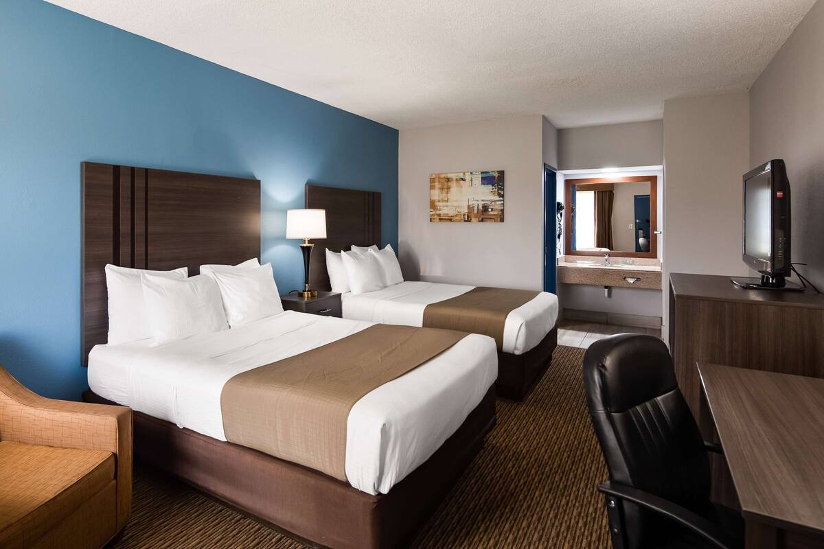 A hotel room with two beds, a desk, a chair, a TV, and artwork on the walls.