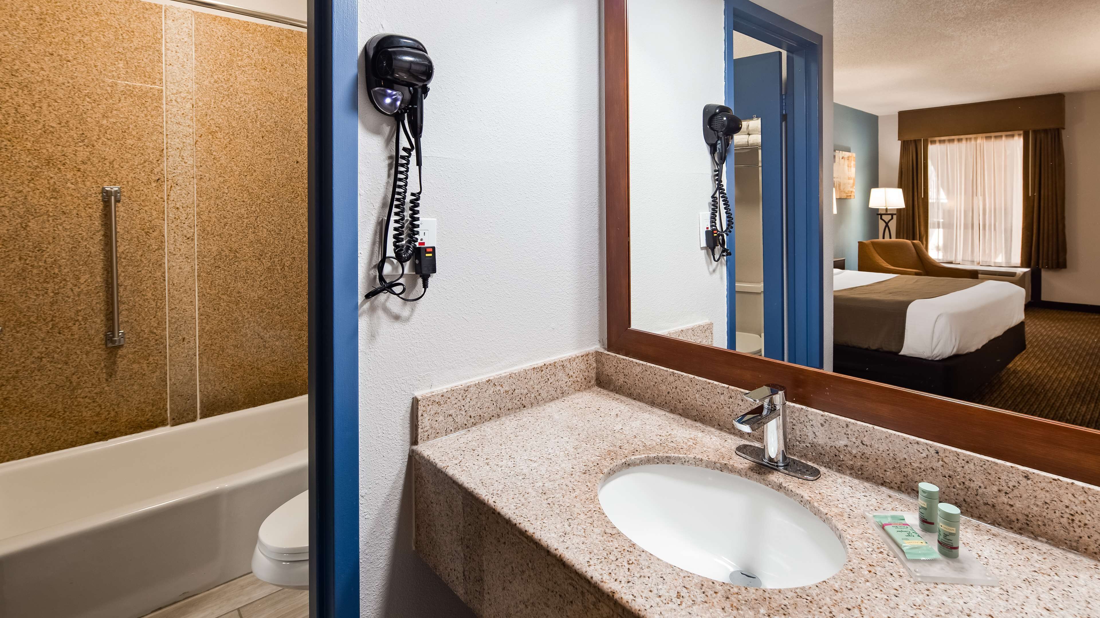 A hotel bathroom with a sink, mirror, hairdryer, and shower.
