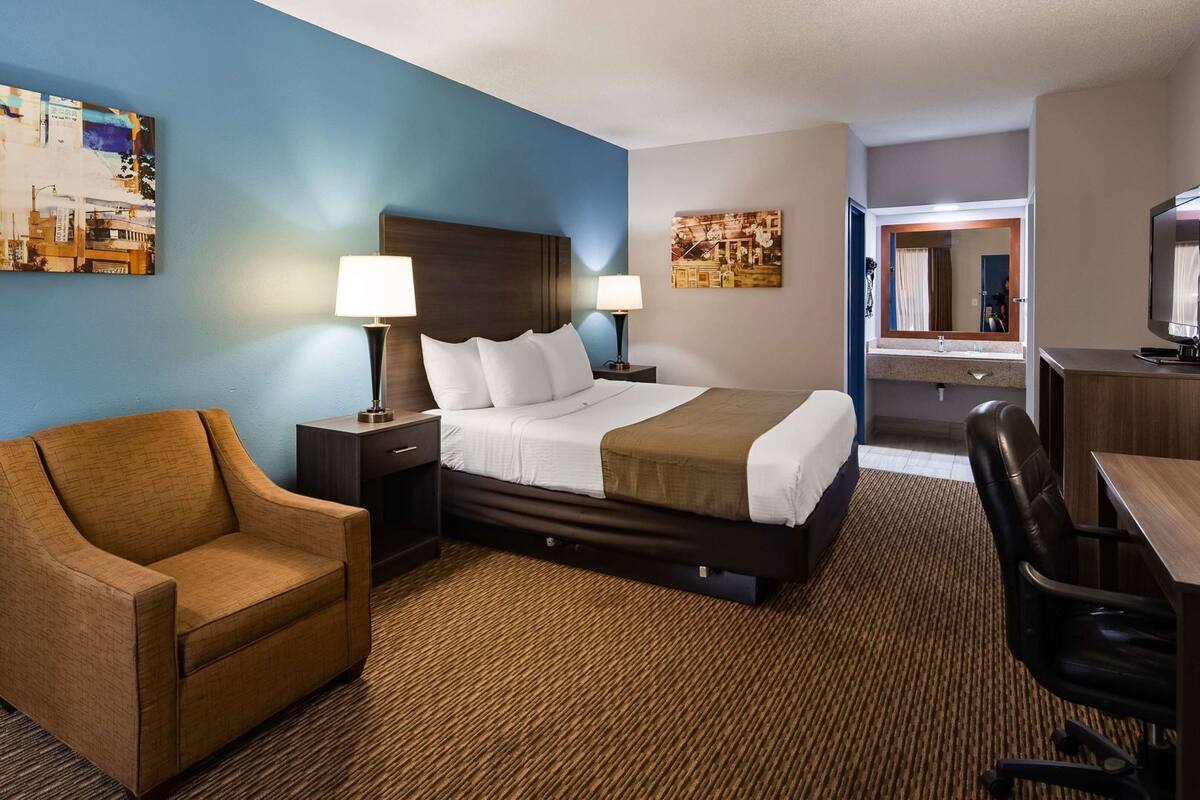 A hotel room with a bed, a chair, a desk, and a television.