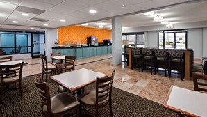 A hotel dining area with tables and chairs, a kitchen area with a counter, and a view of the outside. - Best Western Emporia (Emporia)