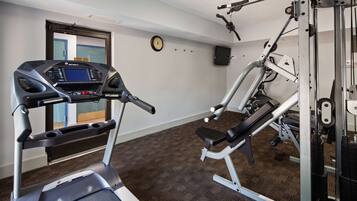 A gym with a treadmill, weight bench, and cable machine.