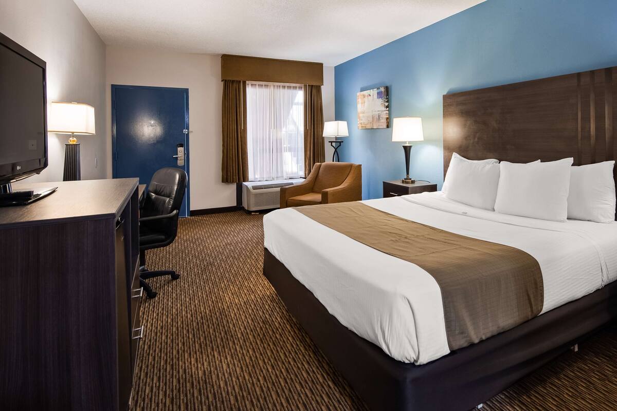 A hotel room with a large bed, a desk with a TV, a chair, and two bedside tables with lamps.