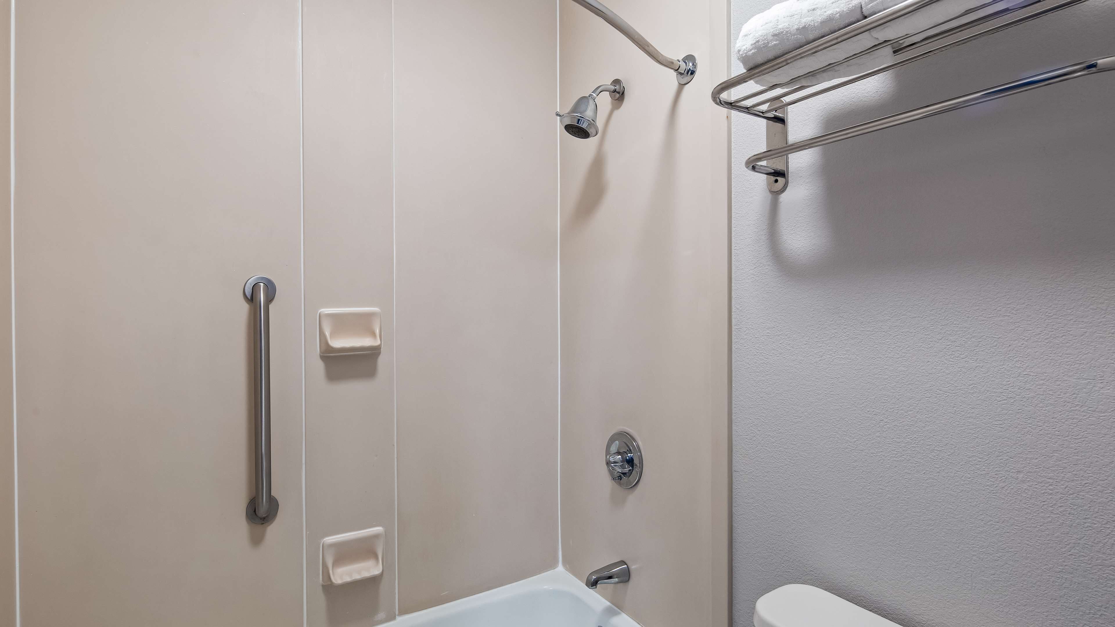 A bathroom with a shower, grab bars, a towel rack, and a toilet.