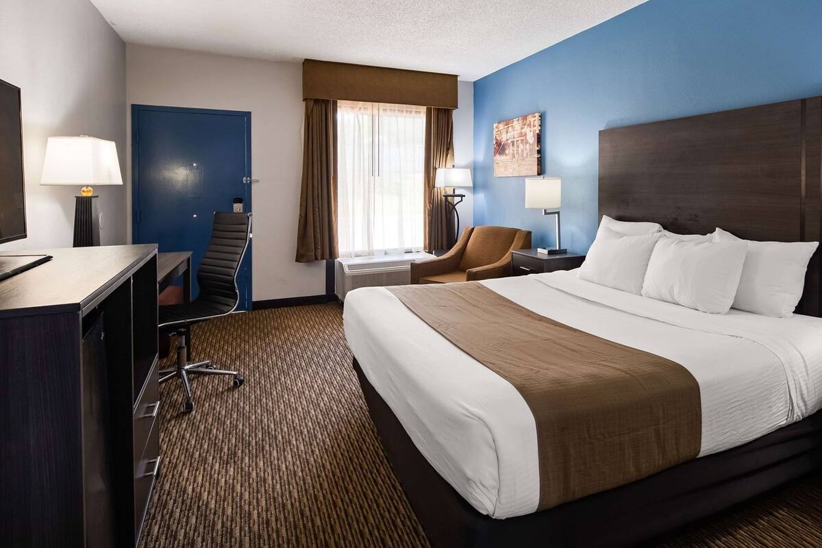 A hotel room with a large bed, a desk, a chair, and a window with curtains.