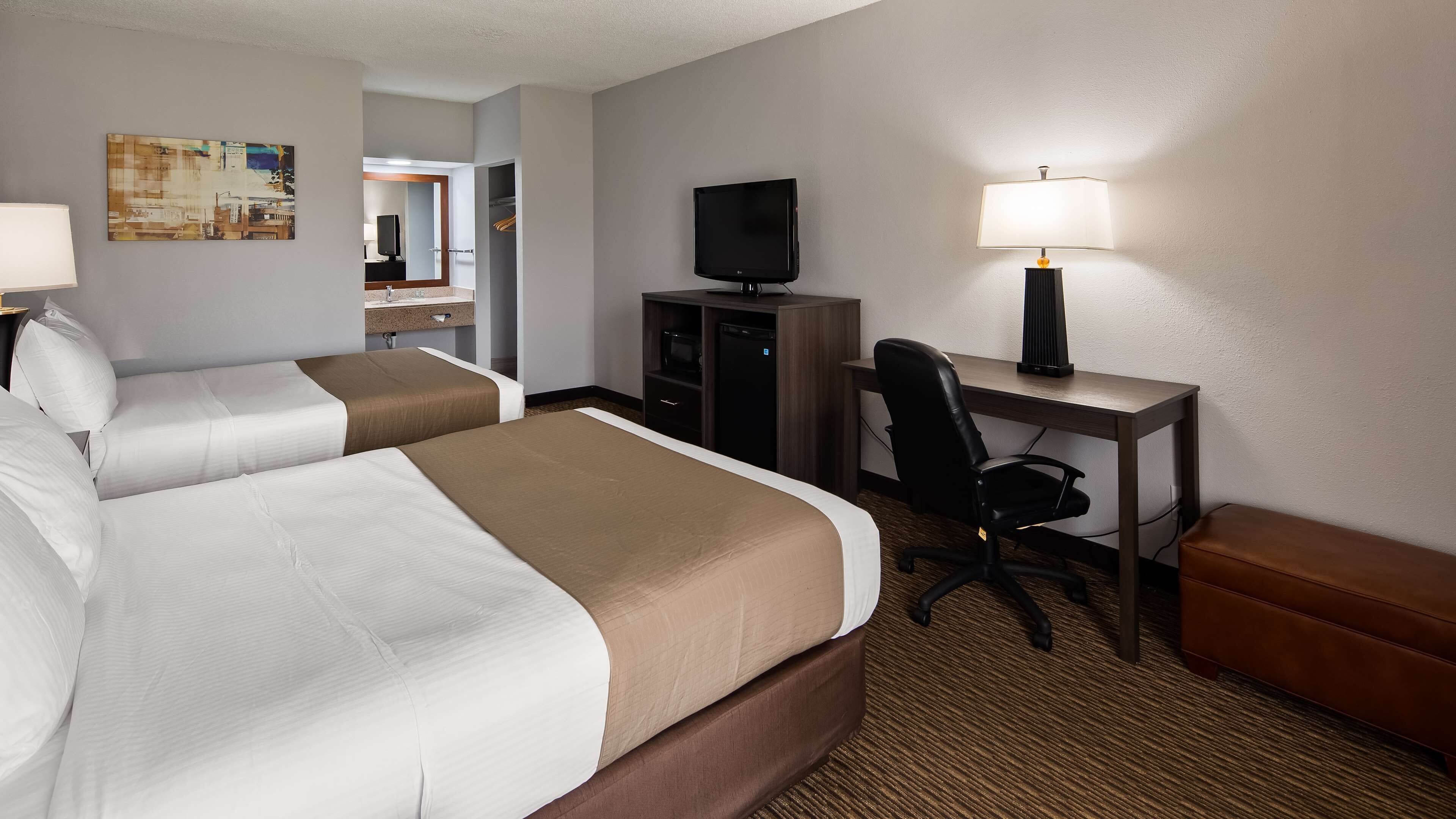 A hotel room with two beds, a desk with a computer, a TV, and a lamp.