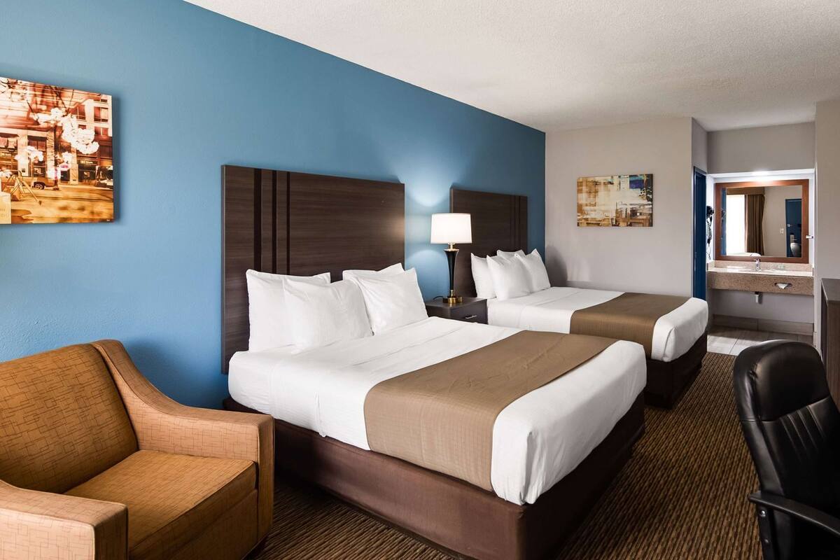 A hotel room with two beds, a desk, a chair, a television, and artwork on the walls.