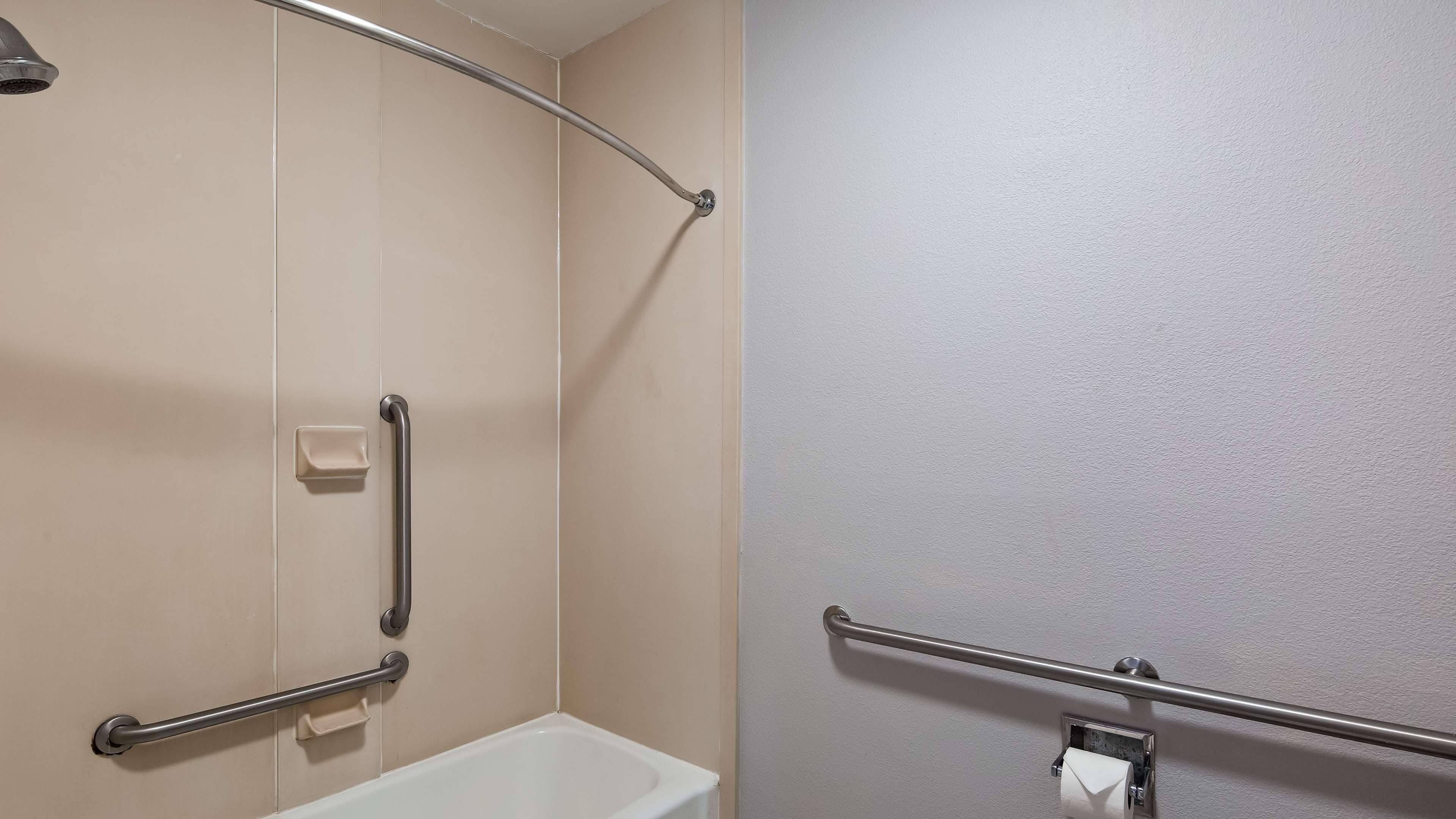 A bathroom with a bathtub, a shower area, and a toilet. There are grab bars installed near the toilet and shower.
