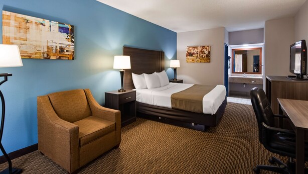 A hotel room with a bed, two bedside tables with lamps, a brown armchair, a desk with a chair, and artwork on the walls. - Best Western Emporia (Emporia)