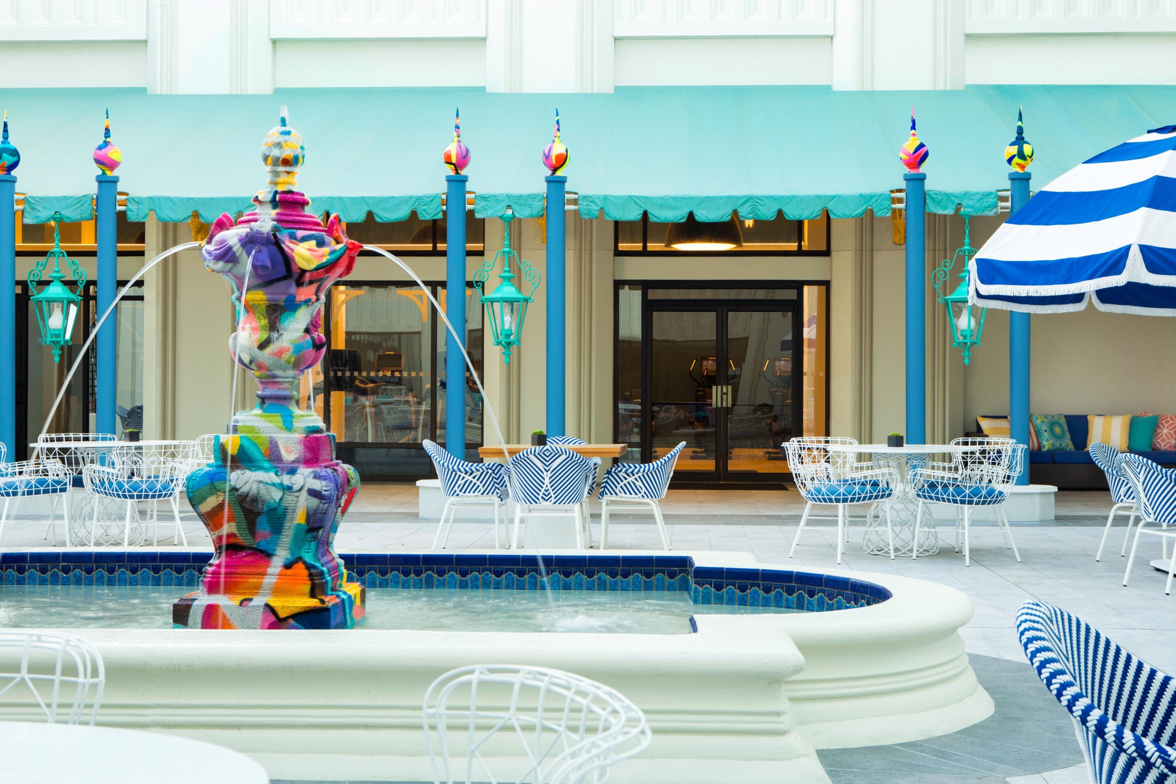 Una fuente colorida en un patio con asientos al aire libre y la entrada de un edificio al fondo.