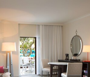 A hotel room with a dining area, a large window with curtains, a round mirror, and a view of an outdoor pool area. - Hilton Orlando Buena Vista Palace - Disney Springs® Area (Lake Buena Vista)