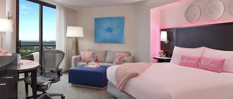 A hotel room with a large bed, a desk, a chair, a sofa, and a view of the outdoors.