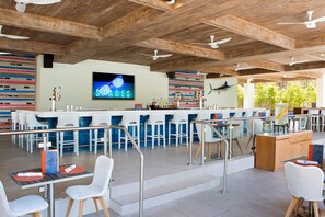 An outdoor bar area with a wooden ceiling, bar stools, and a television screen displaying 'SHADE DES'. - Hilton Orlando Buena Vista Palace - Disney Springs® Area (Lake Buena Vista)