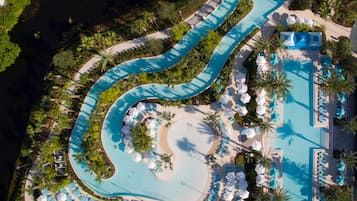 Vista aérea de um resort com piscina sinuosa, espreguiçadeiras e palmeiras.