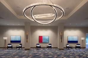 Un hall d’hôtel doté d’un grand lustre circulaire, de plusieurs espaces aménagés pour s’asseoir et d’œuvres d’art abstraites accrochées aux murs.