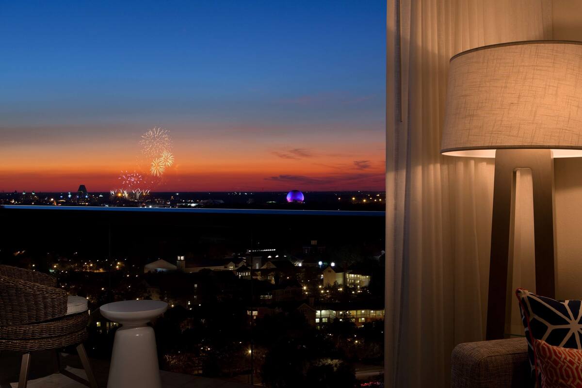 Un balcone con vista sullo skyline cittadino al crepuscolo, con fuochi d'artificio e una struttura a cupola viola.