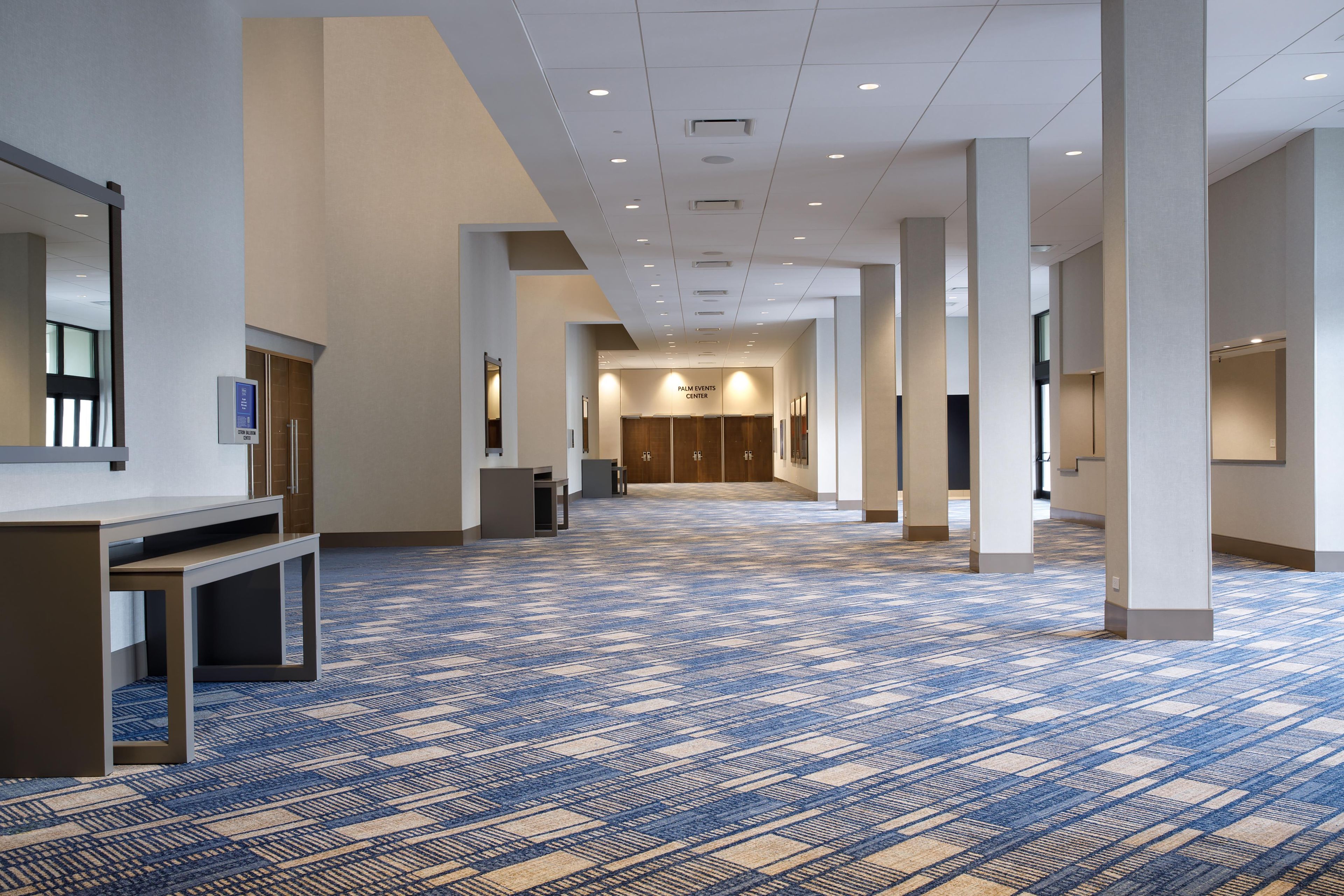 Pasillo de hotel con alfombra estampada, mostrador de recepción y un cartel para el Palm Events Center.