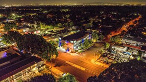 Vista aérea de un paisaje urbano nocturno con edificios iluminados, calles y una cadena montañosa distante.
