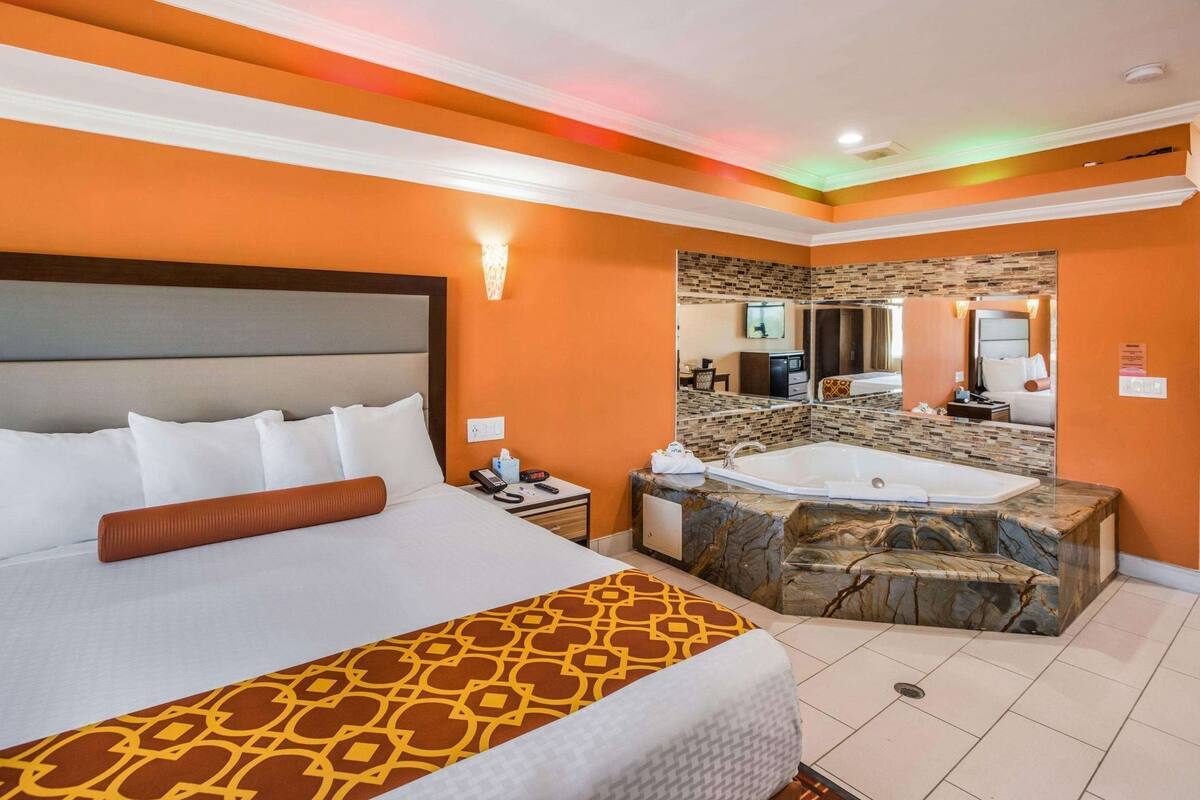 Een hotelkamer met een groot bed, een badkamer met een badkuip, en een spiegel die de kamer weerkaatst.