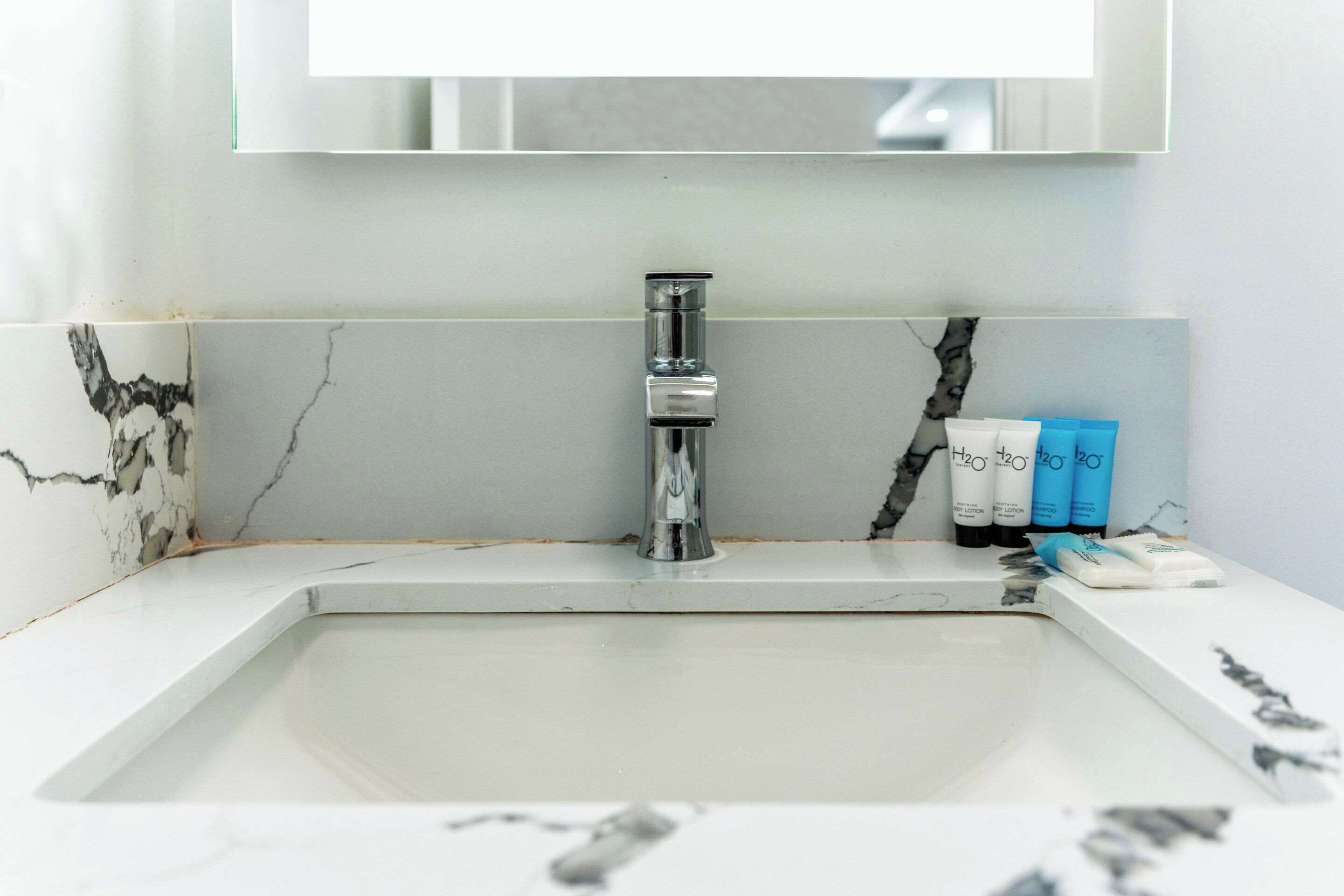 A bathroom with a white sink, a mirror above it, and toiletries on the counter.