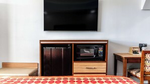 Habitación de hotel con cama, televisor montado en la pared, microondas y refrigerador integrados en un mueble de madera.